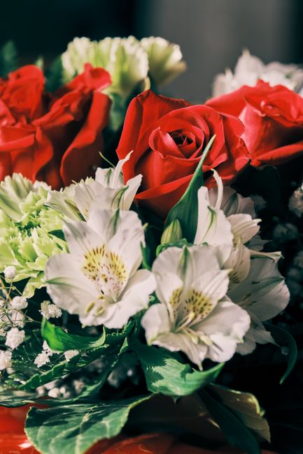 A close-up of a floral arrangement featuring vibrant red roses with tightly layered petals, complemented by white Alstroemeria flowers with delicate, speckled yellow centers and soft green leaves. The