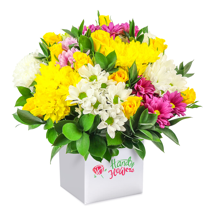 A lush, rounded bouquet of cheerful mixed flowers rises generously from a clean white square gift box, set against a bright, uncluttered white backdrop that emphasises every colour and texture. At first glance, the arrangement radiates happy energy, dominated by rich yellows, clear whites, and vivid fuchsia tones woven harmoniously together. Large yellow chrysanthemums form the core, their many-layered petals creating a cushiony surface that looks almost velvety to the touch, while clusters of small yellow roses, some tightly furled, cluster around them like miniature suns. These warm shades are balanced by a scattering of pure white chrysanthemums, both daisy-like with distinct green centres and fuller, pompom-style blooms that provide bulk and a sense of softness, like drifting clouds over Barnsbury's tree-lined streets. Threading between the yellow and white flowers are bold fuchsia and magenta chrysanthemums, their saturated hues giving the design a confident, modern edge. Some petals show lighter pink highlights, introducing subtle variation that keeps the eye moving across the bouquet. Delicate pink and yellow rosebuds appear here and there, suggesting unfolding stories and adding a sweet, intimate note. Surrounding the flowers, deep green foliage-likely sturdy, glossy leaves similar to ruscus-provides strong structure and a polished frame. The leaves peek out between blossoms and ring the base of the dome, intensifying the brightness of the petals through contrast. All of this sits neatly in a white cube box, minimalist and contemporary, making the design feel gift-ready and easy to place in any Barnsbury flat or office. It's the sort of affordable, mixed arrangement you might choose for a birthday tea at home, a small celebration in a Barnsbury café, or simply to bring a burst of colour to an otherwise quiet weekday.